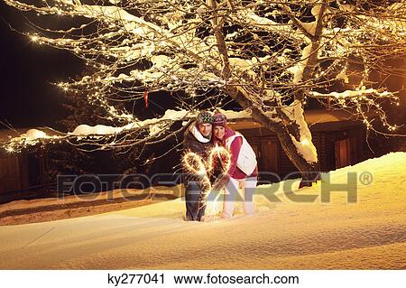 Stock Image - Young couple making heart shape with sparkler by night. Fotosearch