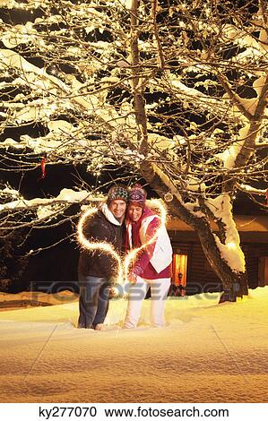 Stock Image - Young couple making heart shape with sparkler by night. Fotosearch