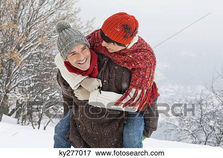 Stock Photo - Young man giving his girlfriend piggyback in snow. Fotosearch