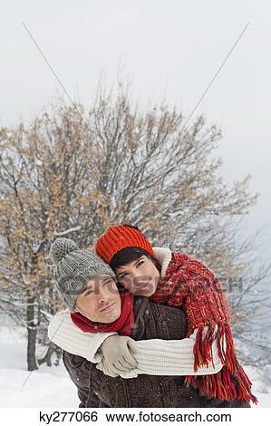 Stock Photograph - Young man giving his girlfriend piggyback in snow. Fotosearch