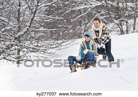Stock Photo - Young man pushing woman on sled. Fotosearch