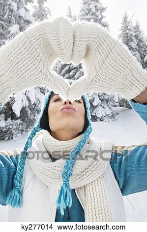Picture - Young woman in winter clothes making heart shape with hands. Fotosearch