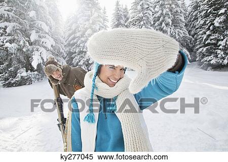 Young woman in winter clothes smiling at camera, man holding skis in background View Large Photo Image Stock Photography - Young woman in winter clothes smiling at camera, man holding skis in background. Fotosearch