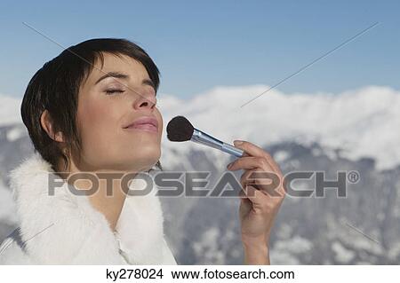 Young woman applying make-up, mountains in background View Large Photo Image Picture - Young woman applying make-up, mountains in background. Fotosearch