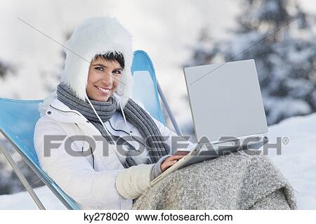 Stock Image - Young woman using laptop computer in snow. Fotosearch