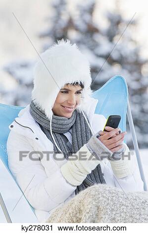 Stock Image - Young woman using mobile phone in snow. Fotosearch