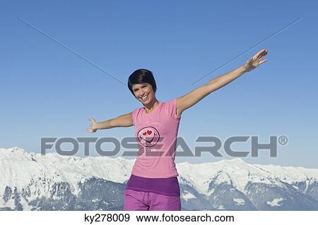 Young woman with arms raised, smiling at camera, mountains in background View Large Photo Image Stock Photo - Young woman with arms raised, smiling at camera, mountains in background. Fotosearch