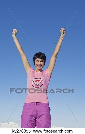 Young woman with arms raised, smiling at camera, mountains in background View Large Photo Image Stock Photography - Young woman with arms raised, smiling at camera, mountains in background. Fotosearch