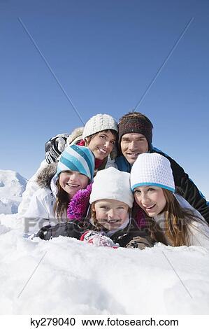 Stock Image - Happy family lying in snow, smiling at camera. Fotosearch