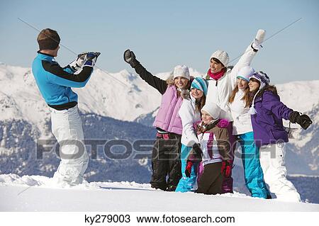 Stock Image - Man taking picture of family in snow. Fotosearch