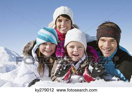 Stock Image - Parents and children lying in snow, smiling at camera. Fotosearch