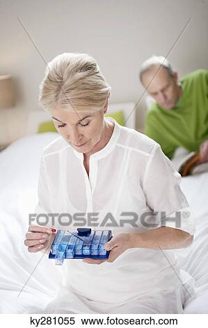 Woman taking a capsule with her husband behind her View Large Photo Image Stock Photography - Woman taking a capsule with her husband behind her. Fotosearch