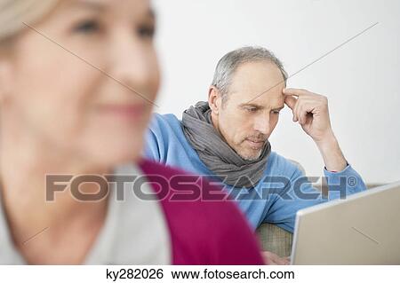 Close-up of a woman with a man working on a laptop in the background View Large Photo Image Stock Photograph - Close-up of a woman with a man working on a laptop in the background. Fotosearch