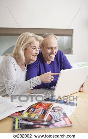 Couple looking at a laptop and smiling View Large Photo Image Stock Image - Couple looking at a laptop and smiling. Fotosearch