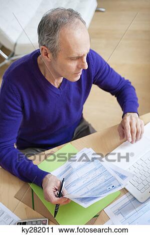 Stock Image - Man holding tax forms and using a laptop. Fotosearch
