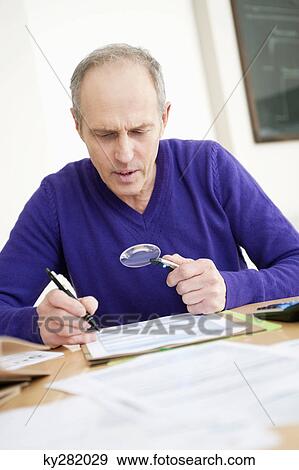 Man looking through a magnifying glass while filling his tax form View Large Photo Image Stock Photo - Man looking through a magnifying glass while filling his tax form. Fotosearch