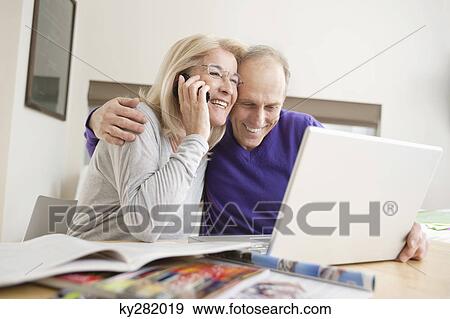 Woman talking on a mobile phone sitting with her husband in front of a laptop View Large Photo Image Stock Photo - Woman talking on a mobile phone sitting with her husband in front of a laptop. Fotosearch