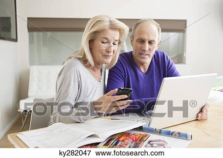 Stock Photo - Woman text messaging on a mobile phone with her husband sitting beside her. Fotosearch