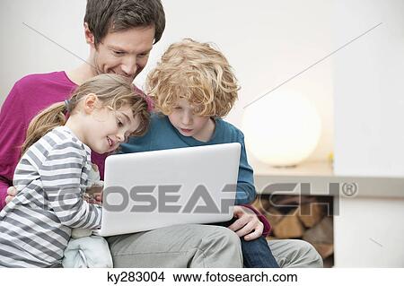 Picture - Close-up of a man assisting his son and daughter in using a laptop. Fotosearch