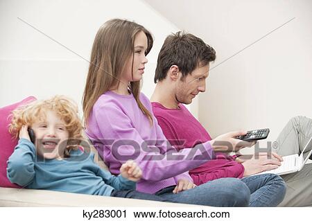 Family sitting together involved in different activities View Large Photo Image Stock Image - Family sitting together involved in different activities. Fotosearch