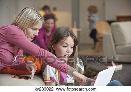 Stock Image - Woman assisting her daughter in using a laptop. Fotosearch
