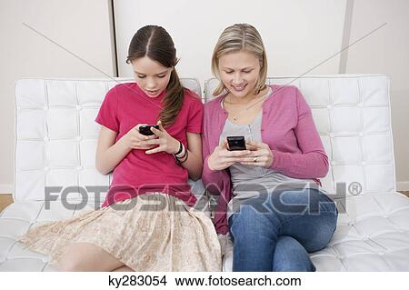 Woman with her daughter text messaging on mobile phones View Large Photo Image Picture - Woman with her daughter text messaging on mobile phones. Fotosearch