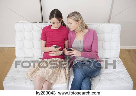 Woman with her daughter text messaging on mobile phones View Large Photo Image Stock Image - Woman with her daughter text messaging on mobile phones. Fotosearch