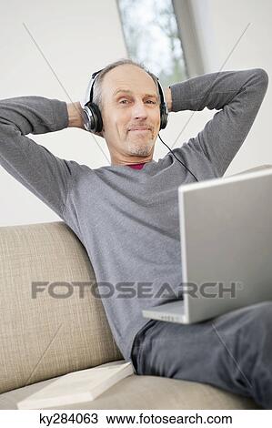 Man using a laptop and listening to music View Large Photo Image Stock Image - Man using a laptop and listening to music. Fotosearch
