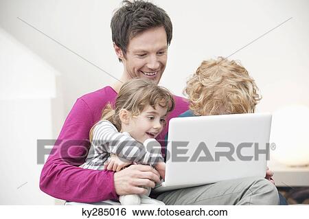 Stock Photograph - Close-up of a man assisting his son and daughter in using a laptop. Fotosearch