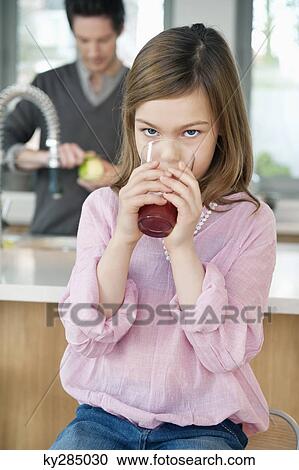 Stock Image - Girl drinking juice with her father standing behind her. Fotosearch