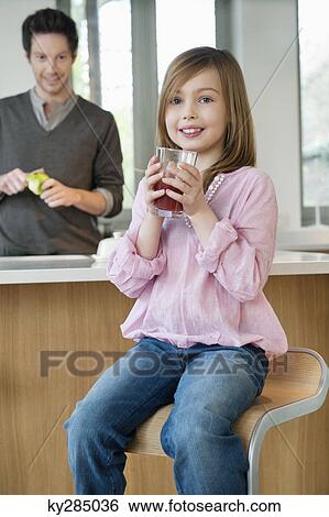 Stock Photograph - Girl drinking juice with her father standing behind her. Fotosearch