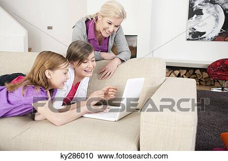 Two girls using a laptop on a couch with their grandmother standing beside them View Large Photo Image Stock Image - Two girls using a laptop on a couch with their grandmother standing beside them. Fotosearch