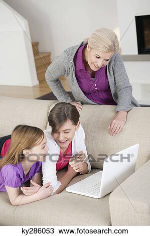 Two girls using a laptop on a couch with their grandmother View Large Photo Image Stock Image - Two girls using a laptop on a couch with their grandmother. Fotosearch