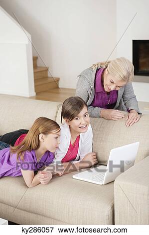 Two girls using a laptop on a couch with their grandmother standing beside them View Large Photo Image Stock Photo - Two girls using a laptop on a couch with their grandmother standing beside them. Fotosearch