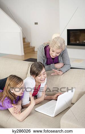 Two girls using a laptop on a couch with their grandmother standing beside them View Large Photo Image Stock Photograph - Two girls using a laptop on a couch with their grandmother standing beside them. Fotosearch