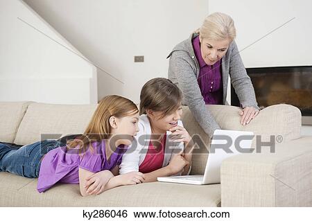 Two girls using a laptop on a couch with their grandmother View Large Photo Image Stock Photograph - Two girls using a laptop on a couch with their grandmother. Fotosearch