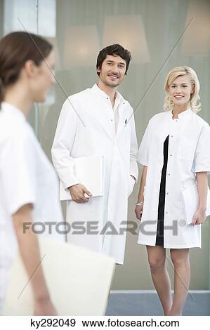 Stock Photo - Male doctor standing with two female doctors. Fotosearch