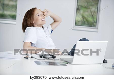 Stock Image - Female doctor sitting in an office and smiling. Fotosearch