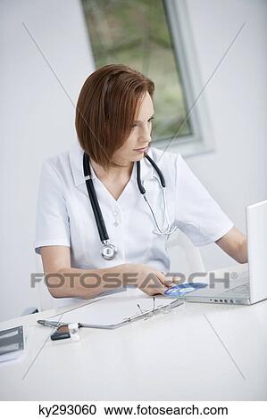 Female doctor sitting in an office inserting CD into a laptop View Large Photo Image Stock Image - Female doctor sitting in an office inserting CD into a laptop. Fotosearch