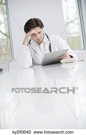 Stock Image - Male doctor examining a medical report and looking upset. Fotosearch