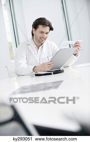Male doctor examining a medical report and smiling View Large Photo Image Stock Image - Male doctor examining a medical report and smiling. Fotosearch