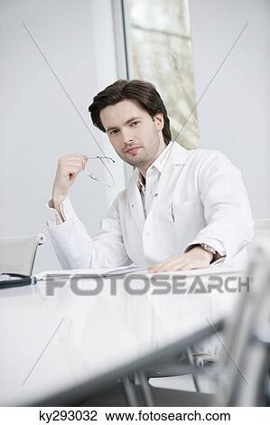 Male doctor sitting in his office View Large Photo Image Stock Image - Male doctor sitting in his office. Fotosearch