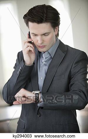 Businessman checking the time and talking on a mobile phone View Large Photo Image Stock Image - Businessman checking the time and talking on a mobile phone. Fotosearch
