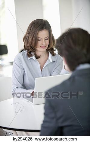 Businesswoman sitting in front of a and businessman working on a laptop View Large Photo Image Stock Photograph - Businesswoman sitting in front of a and businessman working on a laptop. Fotosearch