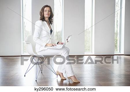 Stock Image - Businesswoman sitting on a chair and using a laptop. Fotosearch