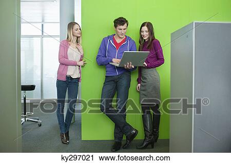 Stock Image - Businessman using a laptop with his colleagues in an office. Fotosearch