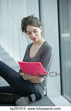 Businesswoman sitting in an office corridor and looking at a file View Large Photo Image Picture - Businesswoman sitting in an office corridor and looking at a file. Fotosearch