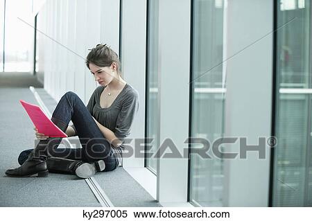 Businesswoman sitting in an office corridor and looking at a file View Large Photo Image Stock Photography - Businesswoman sitting in an office corridor and looking at a file. Fotosearch