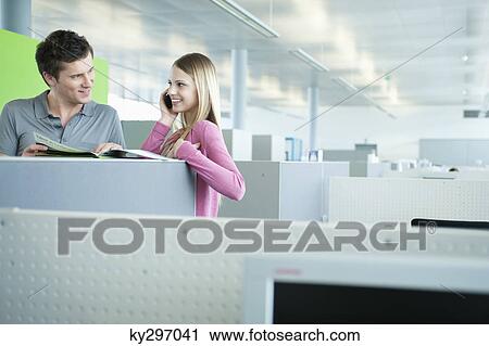Businesswomen talking on a mobile phone while her colleague doing paperwork View Large Photo Image Stock Image - Businesswomen talking on a mobile phone while her colleague doing paperwork. Fotosearch