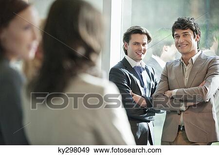 Stock Photo - Two businessmen looking at their female colleagues and smiling. Fotosearch